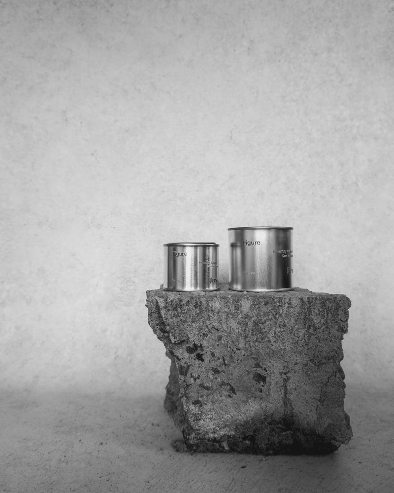  Large and medium sized silver travel tin candle of scent figure wide shot in black and white.