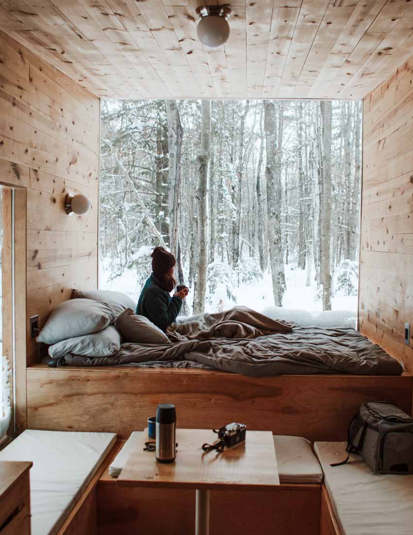 Candle scent image for the fragrance understated beauti. Picture of a cozy cabin looking out to the white snow outside. Feeling cozy and warm inside.