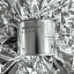 Medium sized silver travel tin candle of fragrance scent understated beauti - close up on metallic background.
