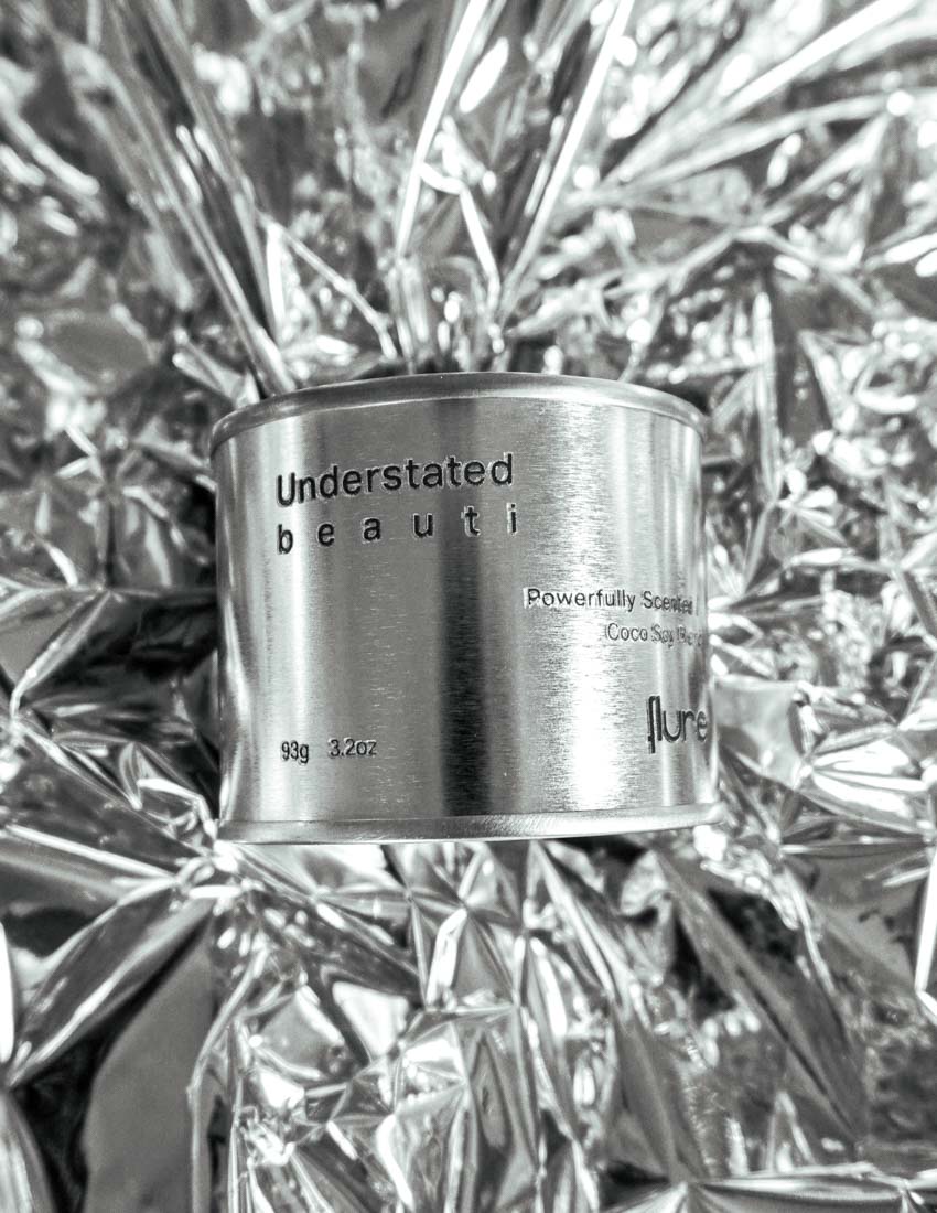 Medium sized silver travel tin candle of fragrance scent understated beauti - close up on metallic background.