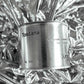 Medium sized silver travel tin candle of fragrance scent toscana - close up on metallic background.