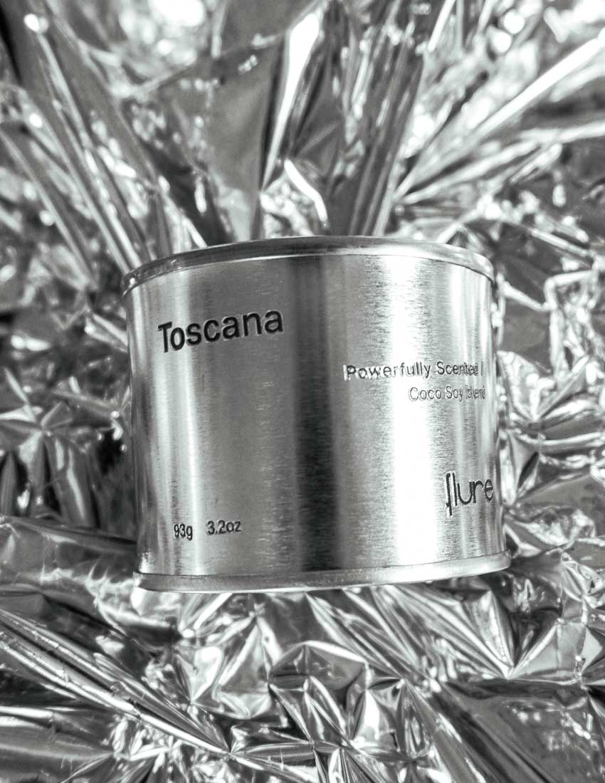 Medium sized silver travel tin candle of fragrance scent toscana - close up on metallic background.