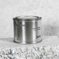 Medium sized silver travel tin candle of fragrance scent toscana - close up on brick.