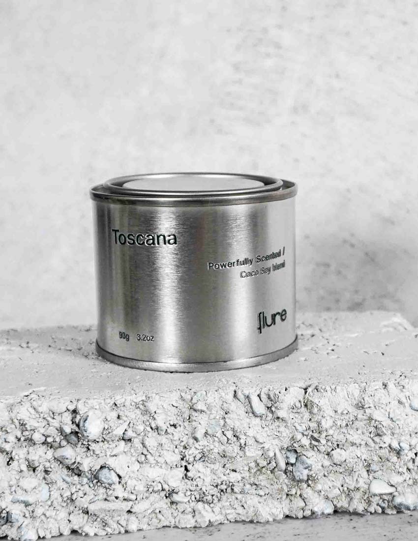 Medium sized silver travel tin candle of fragrance scent toscana - close up on brick.