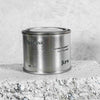 Medium sized silver travel tin candle of fragrance scent toscana - close up on brick.