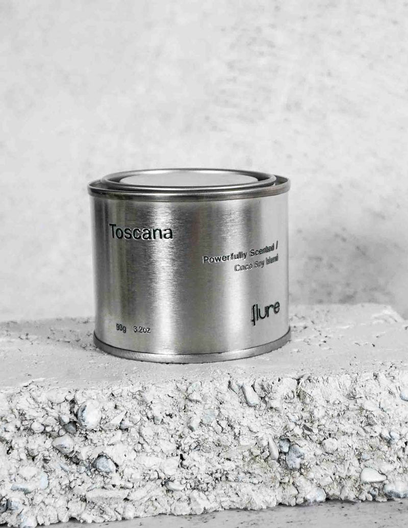 Medium sized silver travel tin candle of fragrance scent toscana - close up on brick.