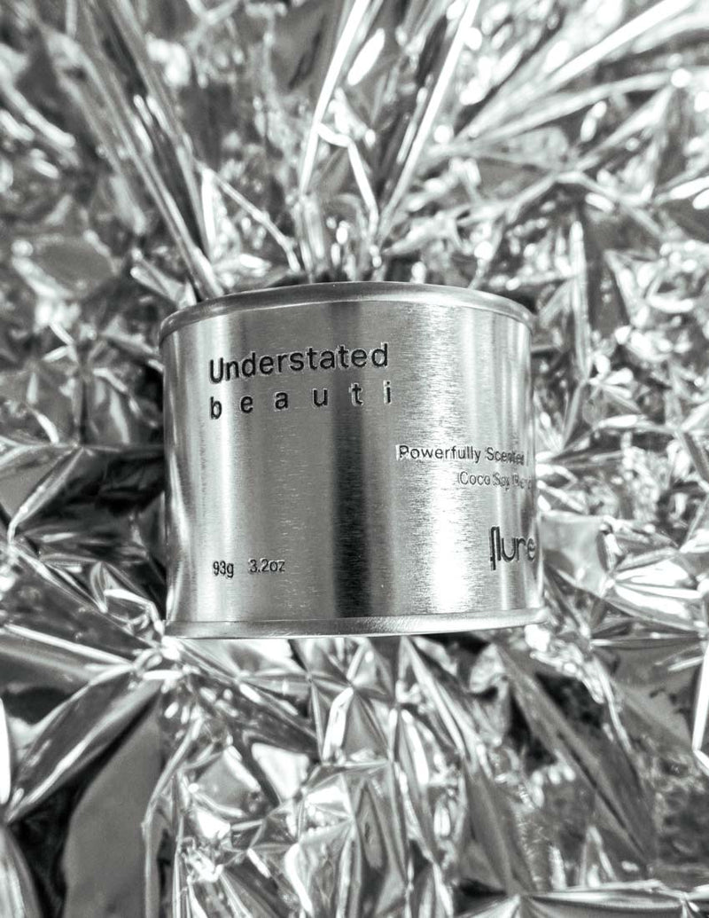 Medium sized silver travel tin candle of fragrance scent understated beauti - close up on metallic background.