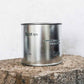 Large sized silver travel tin candle in the fragrance scent spot on - close up on brick.