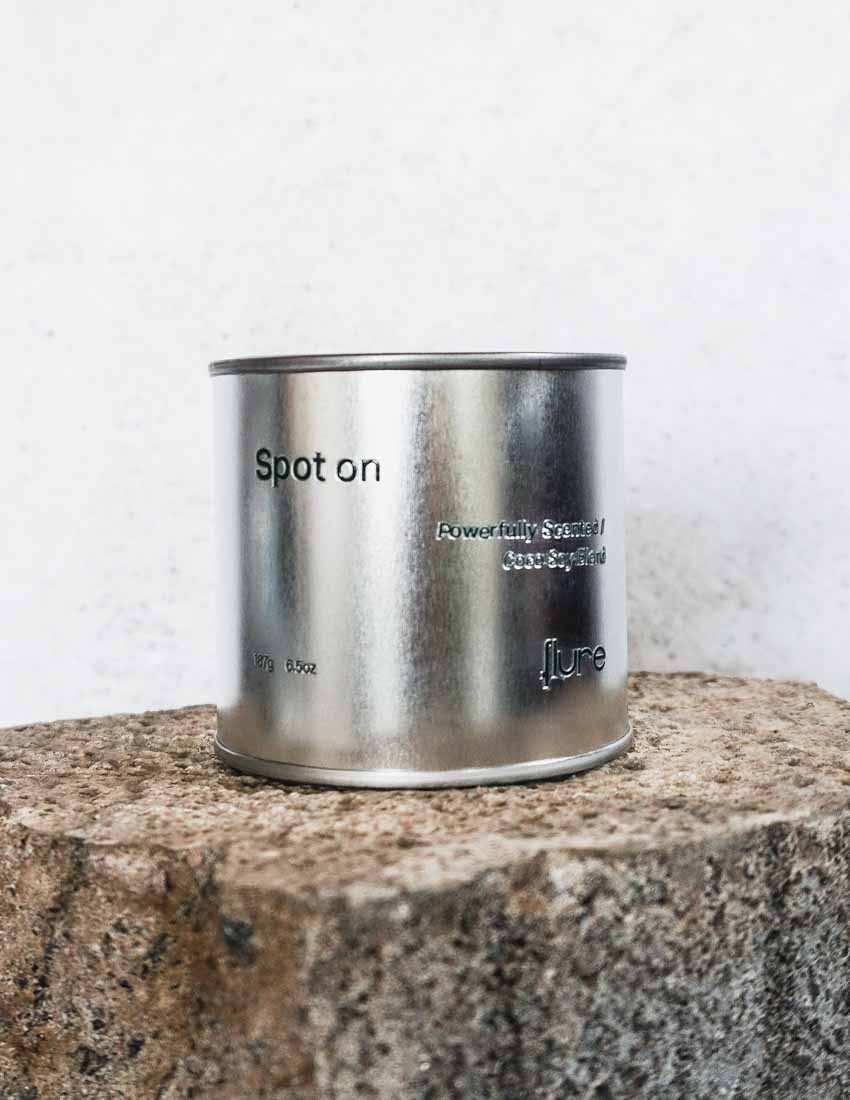 Large sized silver travel tin candle in the fragrance scent spot on - close up on brick.