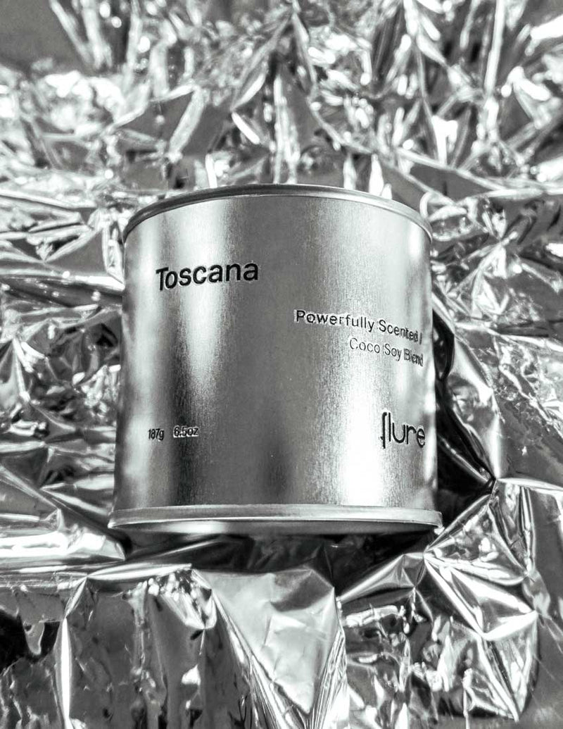 Large sized silver travel tin candle of the fragrance scent toscana - close up on metallic background.